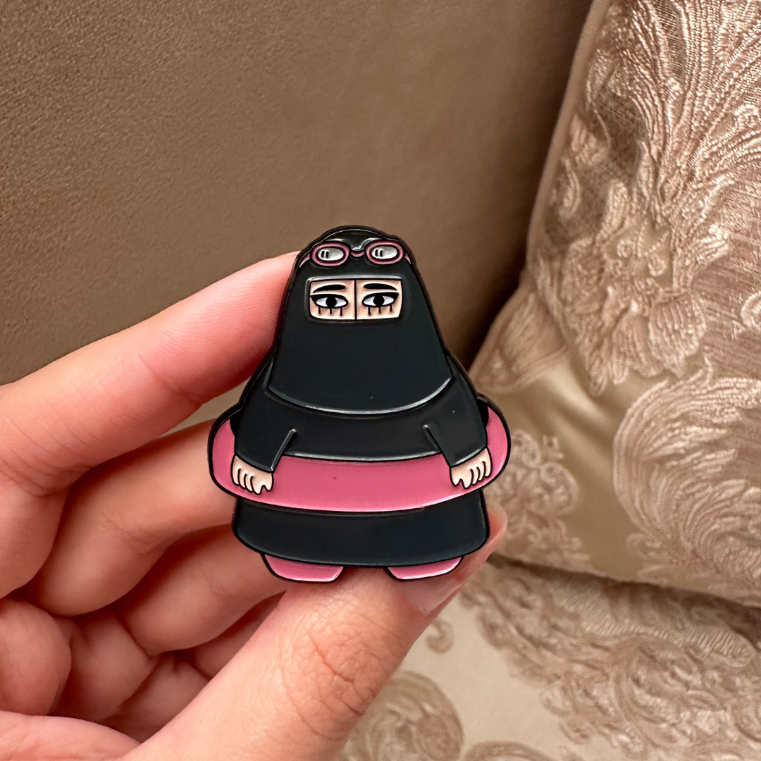 Summer Niqabi Enamel Pin featuring a niqabi woman in a cheerful summery setting. A vibrant accessory perfect for adding cultural flair and a touch of summer fun to jackets, bags, or hats, celebrating the blend of tradition and seasonal joy.